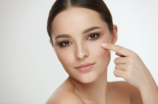 Close-up of a woman pointing to her cheek, showcasing clear skin.